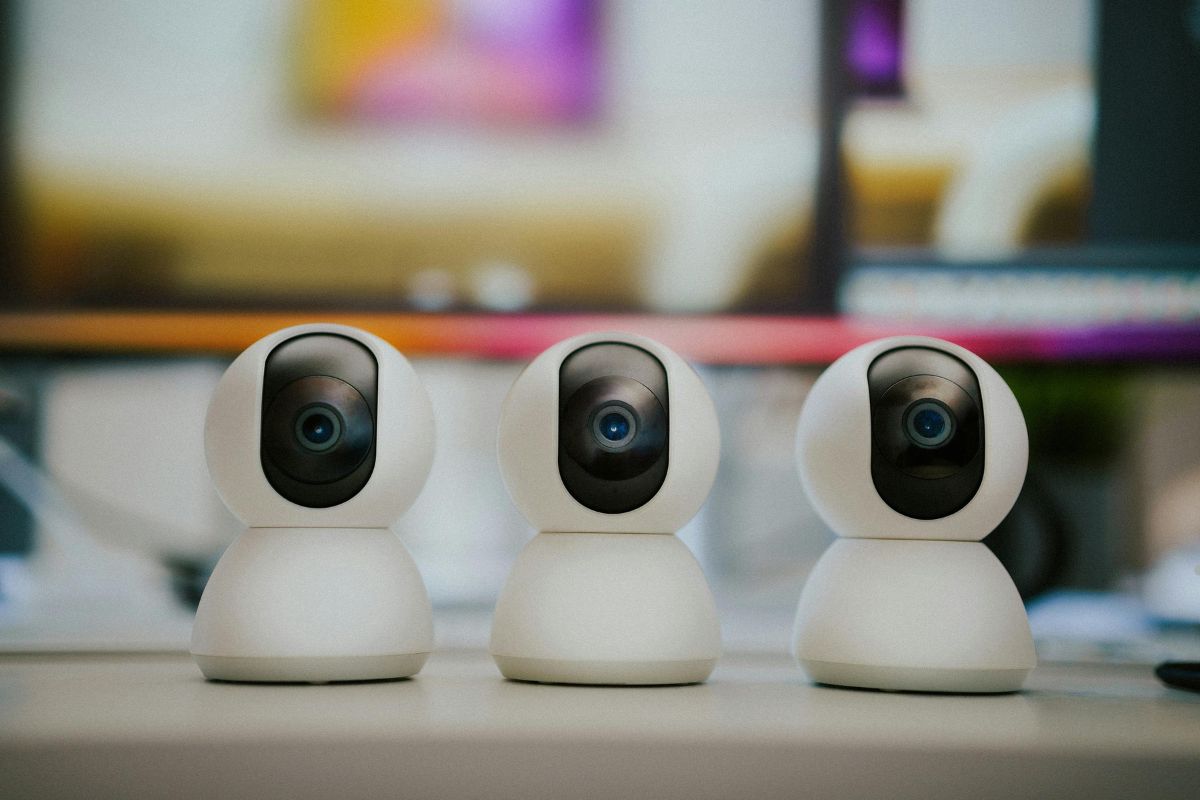 Three modern white security cameras, positioned side by side on a desk, with a blurred background featuring soft colors.
